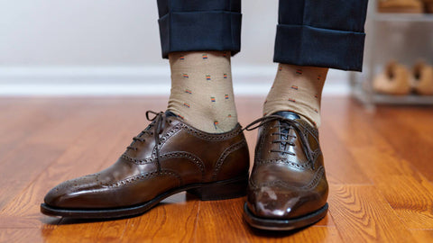 man wearing thin khaki dress socks and dark brown dress shoes while standing on hardwood floor