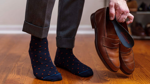 man wearing designer dress socks holding brown luxury loafers