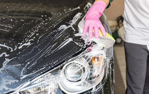 Person wearing pink dishwashing gloves and sponge to clean dirty car 