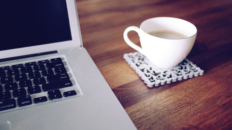 Tea cup on coaster on wood table or desk next to macbook laptop
