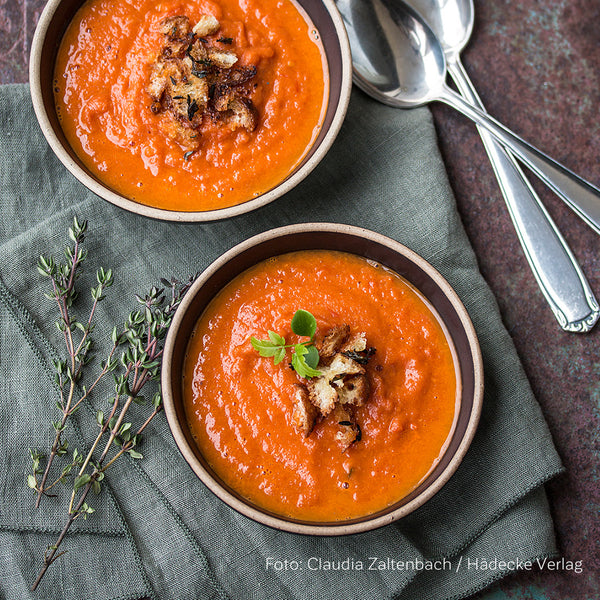 Tomatensuppe gewürzt mit Miso in kleinen Suppenschalen, zwei Löffel, eine graue Tischdecke und Thymian-Zweige