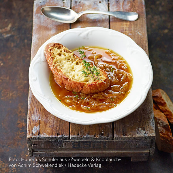 Ein Teller gratinierte Zwiebelsuppe auf einer Holzkiste mit silbernem Löffel © Hubertus Schüler / Hädecke Verlag