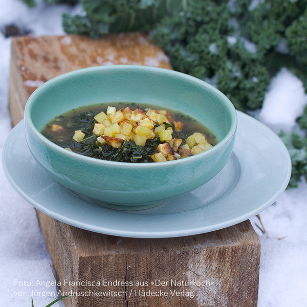 Rezept aus »Der Naturkoch« von Bio-Spitzenkoch Jürgen Andruschkewitsch: Grünkohlsuppe mit glasierten Kartoffeln in winterlicher, verschneiter Landschaft und Grünkohl auf dem Acker im Hintergrund.