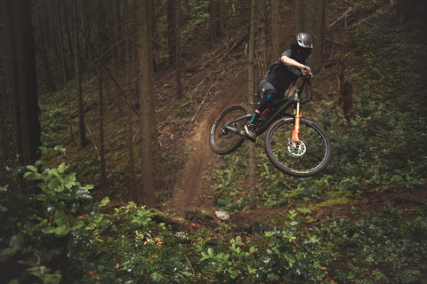 A picture of mountain biker Trevor Thew taking a jump through on his bike through the forest.