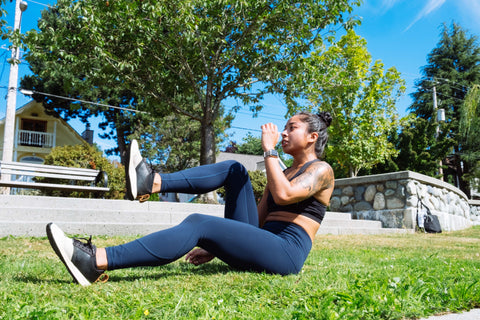 An image of Lanie sitting on the grass in leggings, bringing her knee into her chest.