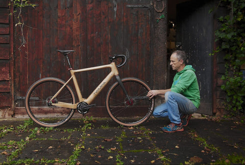 A picture of Andy Dix kneeling in front of his wooden bicycle.