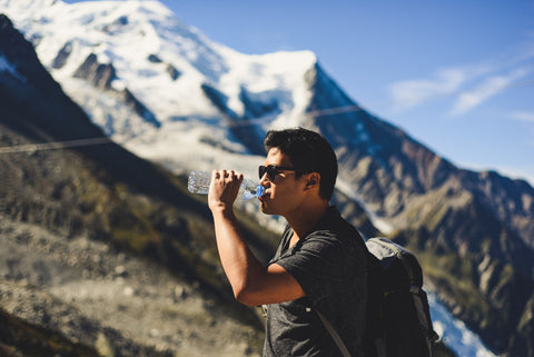 An image of a young Asian man drinking bottled water with mountains in the background.