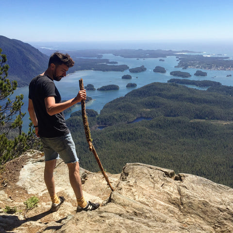 An image of Ollie Cooper, a young white man, on top of a mountain with a walking stick in hand.