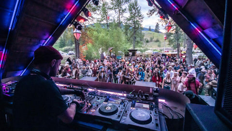 An image of a DJ underneath a tent-like structure as a crowd looks on.