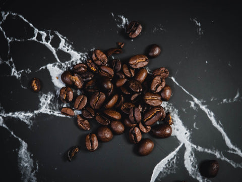 An image of coffee beans spilled across a black and white marble countertop. 