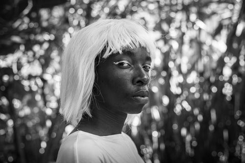 A black and white image showing a Black woman against a glittering backdrop wearing a pale-colored wig and looking directly into the camera.