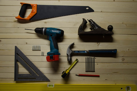 An image of a wood surface where tools — including a saw, drill, hammer, and more — have been arranged in a flat lay style.