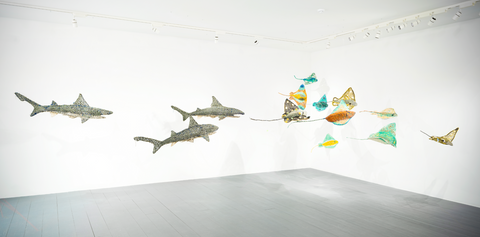 Against white walls and a grey floor, a series of sea life designs have been suspended from the roof including fish and sharks, all made from fishing nets.