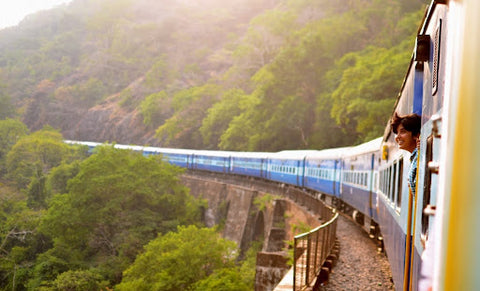 An image of a train passing through the hills and trees with a child sticking their head out of the window.