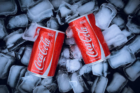 An image of two cans of Coca-Cola resting on a bed of ice.