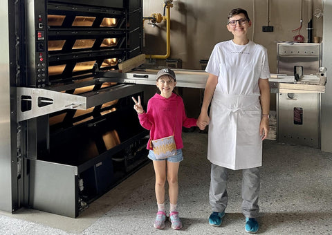 An image of an adult, standing beside a child, in front of a commercial bakery operation.