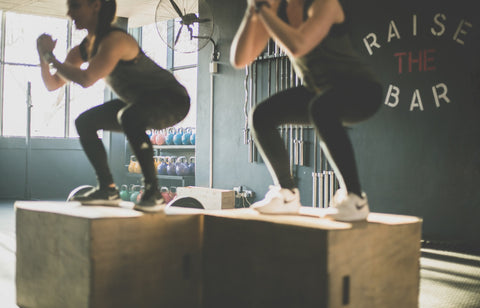 An image of two people jumping up to do box squats in synch. 