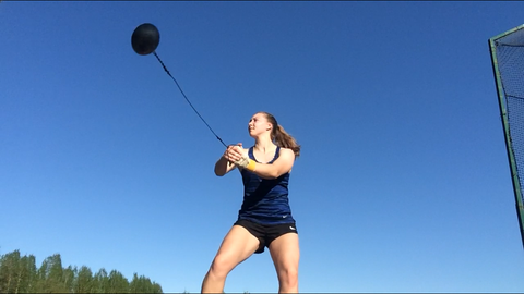 A young woman performs the hammerthrow against a blue sky.