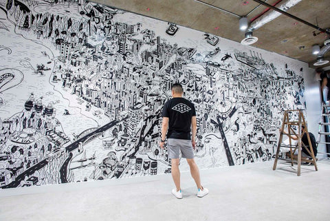A picture of the artist, with his back to the camera, standing in front of one of his murals.