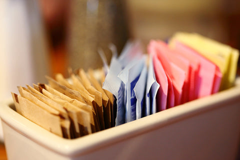 An image of a container of sweetener packets, ranging from brown paper to blue, pink, and yellow.