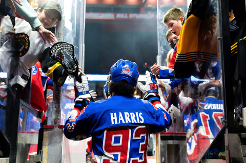 An image of Latrell Harris's back, wearing his Number 93 blue jersey as a row of attendees on either side greet him.