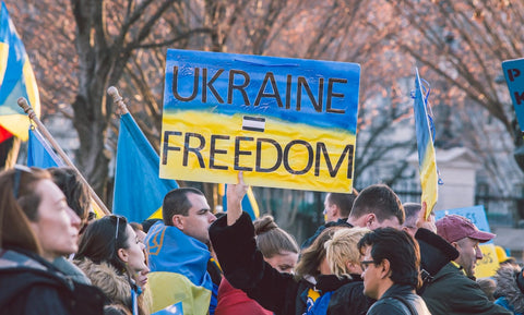 A crowd of people protesting in the streets. One holds up a sign that says Ukraine = Freedom on a blue and yellow background.