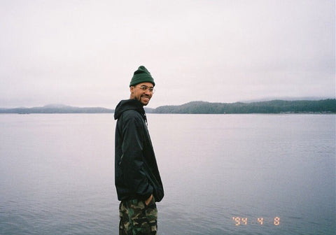 An image of Kody Williams, a young Black man, standing in front of a body of water wearing a toque and smiling at the camera.