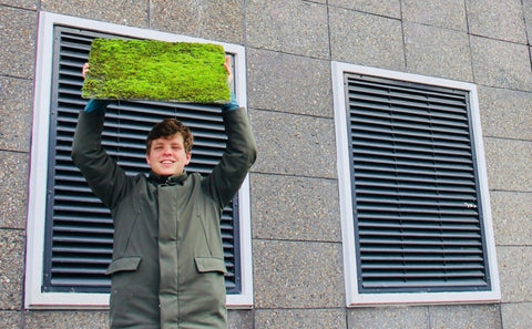 An image of a member of Respyre hoisting a rectangle of moss over his head with a building behind him.