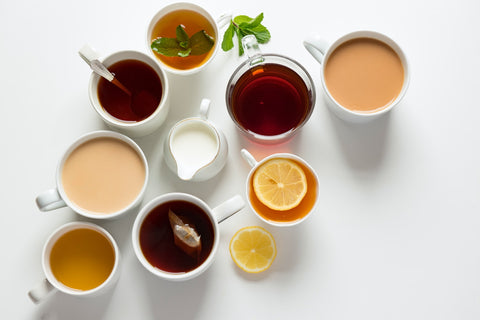 An image of eight cups of tea and coffee placed on a white surface, a white jug of milk sits at the center.