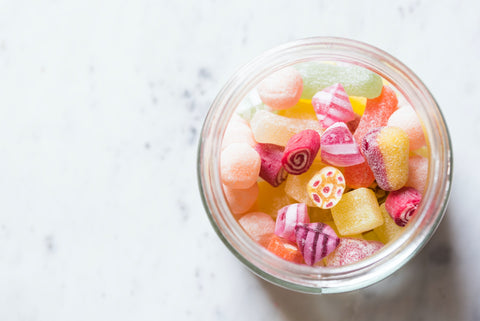 A glass bowl of hard candy is seen from above on an all-white background.