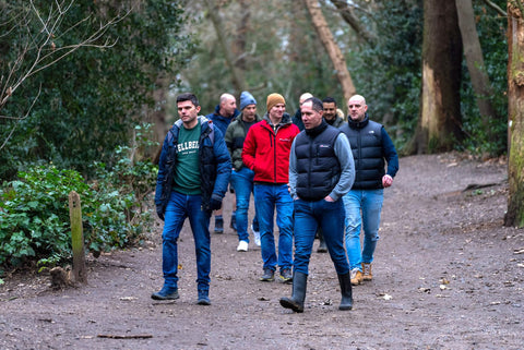 An image of a group of men walking along a forest path, surrounded with trees.