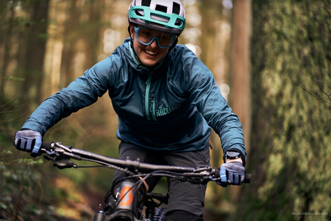 A close-up image of Madeleine on her bike, grinning as she grips the handlebars with the forest in the background.