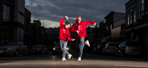 Jacksun and Carlow, two young white men, wearing red hoodies while dancing on the street with a twilight sky in the background.