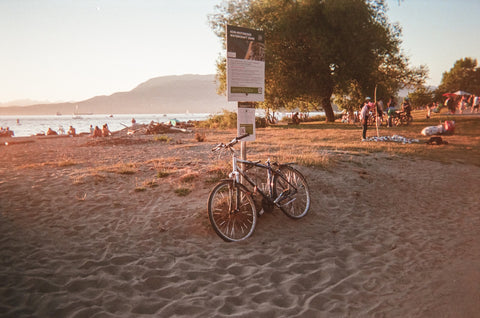 A bike rests against a sign with a beach in the background at sunset.