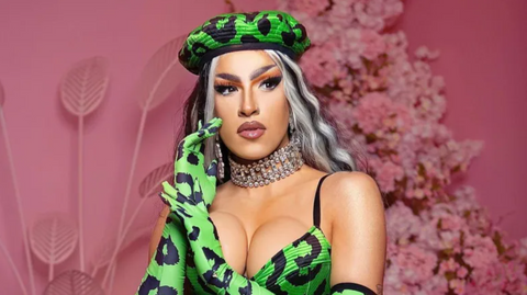 An image of Kendall wearing an acid-green and black outfit, her head resting lightly on her hand with a floral pink background.