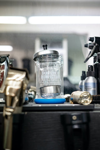 A barber sanitizing and disinfecting jar sitting on a station