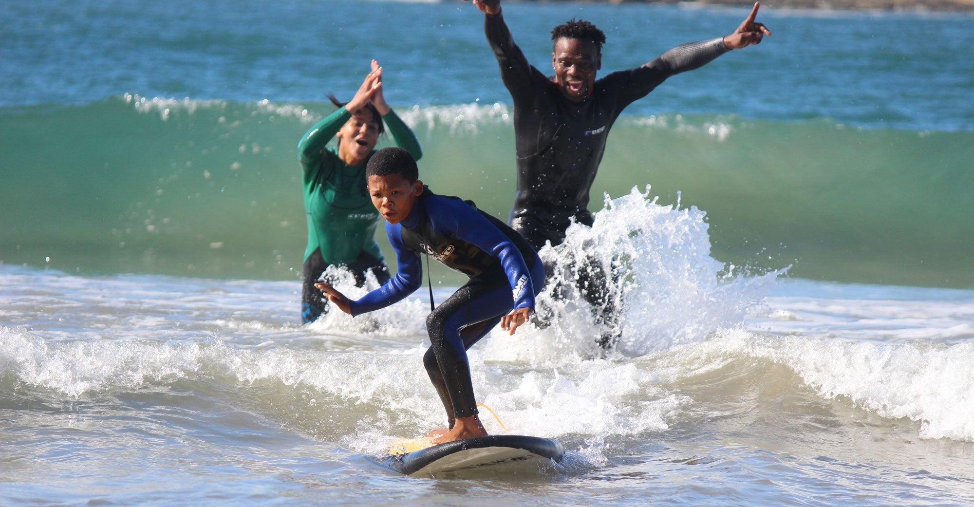 Waves-for-change-participant-catching-a-wave-with-joyful-instructors-behind