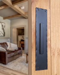 A black steel pull barn door handle on a light wooden door.