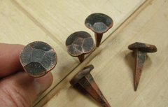 Heavy-duty decorative nails held and positioned over a slab of wood.