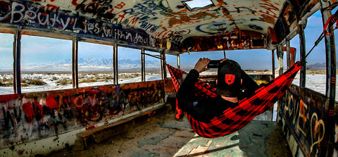 man sitting in a hammock inside of a spray painted bus