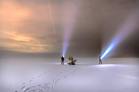 Two people shining flashlights in a snowcovered plain