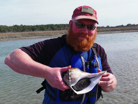 Man with a large, bushy red beard holding a conch shell at Huntington Beach State Park, South Carolina