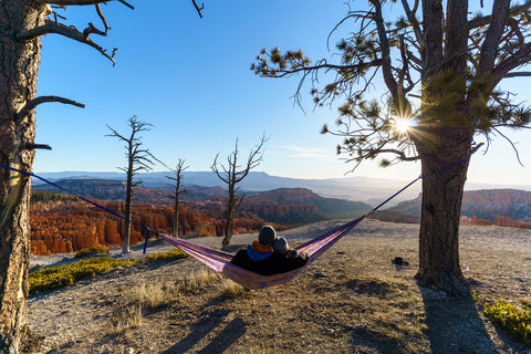 Couple hammocking between two trees overlooking a valley 