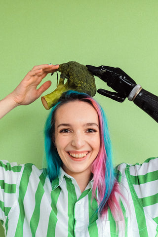 Woman with a prosthetic hand holding a head of broccoli over her head.