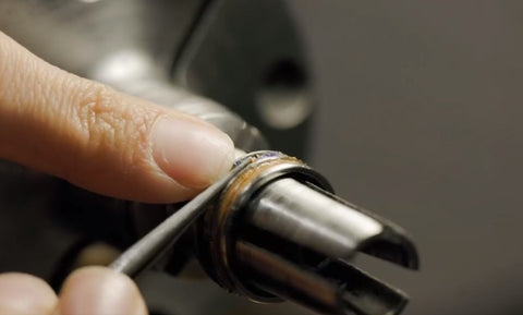 crafter, holding a ring in place on a lathe with left hand thumb, and with right hand uses a tool to inlay the ring with materials