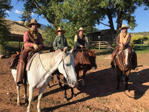 Picture of four people dressed like cowboys posed on horses smiling