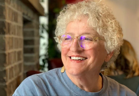 Grandma Darla, a white-haired woman, wearing glasses and a blue shirt, smiling and looking to the left out of frame of the image.