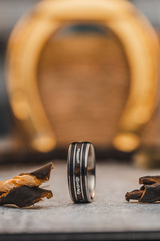 Picture of a custom ring with pieces of leather on either side and a golden horseshoe in the background out of focus