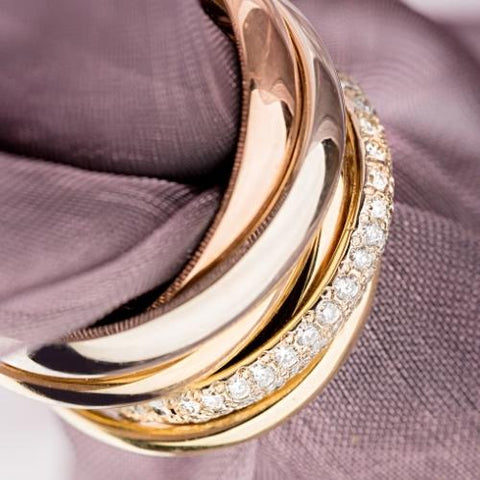 six bands made of different metals, white gold, silver, rose gold, and yellow gold are posed with a piece of taupe tulle running through them. One band is diamond encrusted