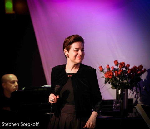 Celia Berk performs with a purple background and roses behind her, wearing red earrings from Icon Style